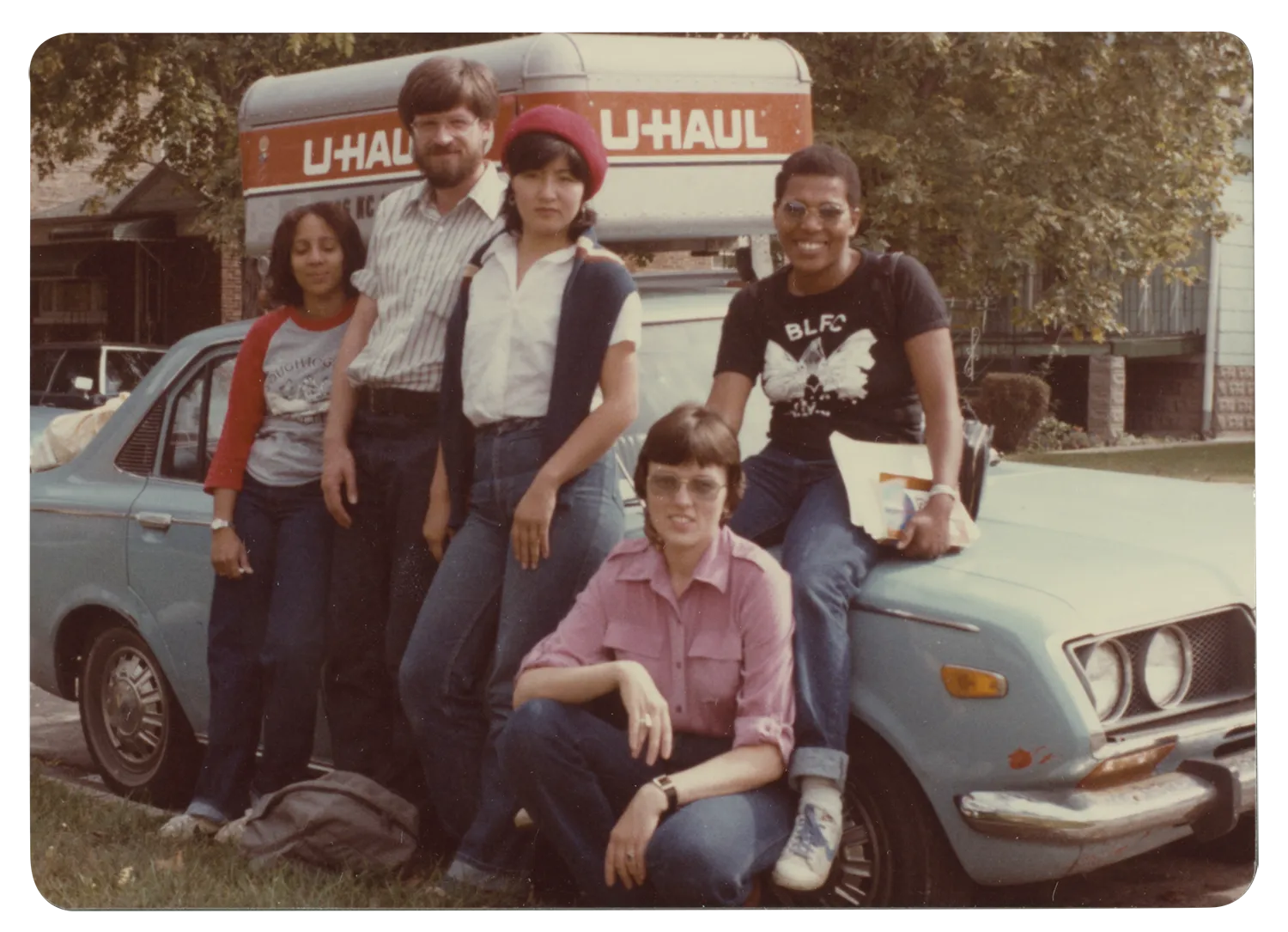 A color photograph of a multiracial group of friends standing in front of a U-Haul truck.