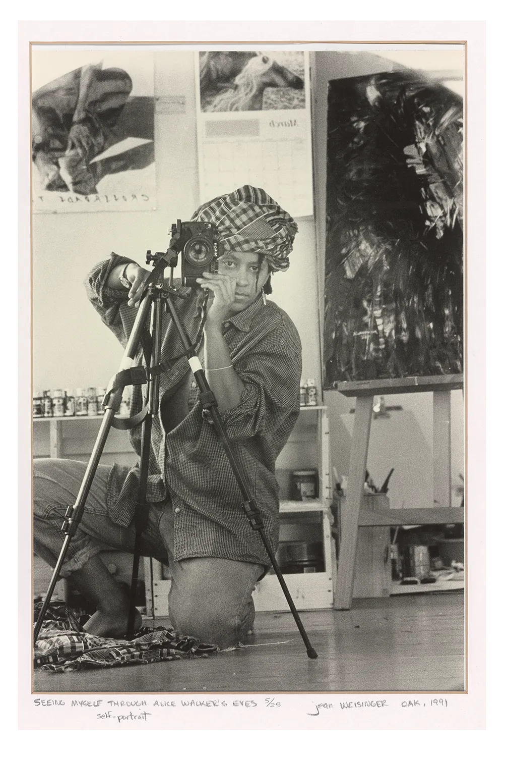 A black-and-white photograph of Alice Walker kneeling behind a camera and looking straight ahead.